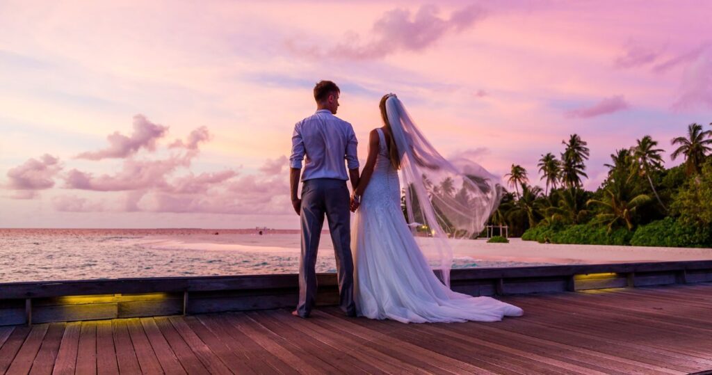 a couple just married in the maldives standing on a dock at sunset