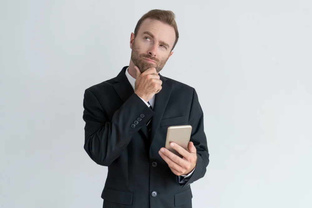 homem de negocio pensativo que toca no queixo pensando e guardando o smartphone